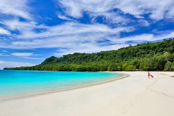 Lady walking down white sand beach with turquoise water