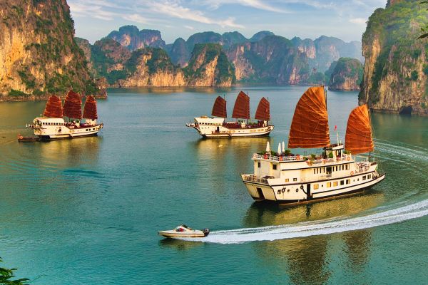 Ships with red sails sailing through tall, close mountains in Vietnam