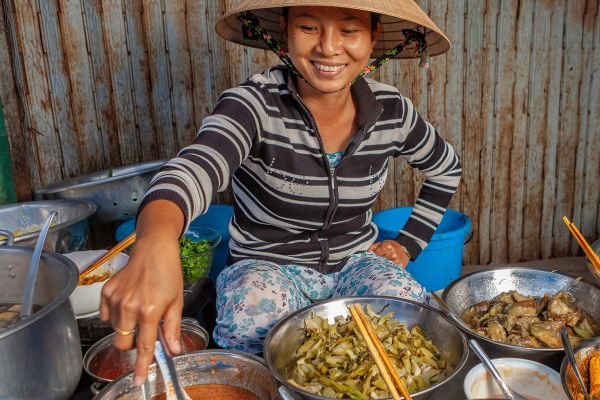 Woman in Vietnam smiling, serving food from several metal bowls