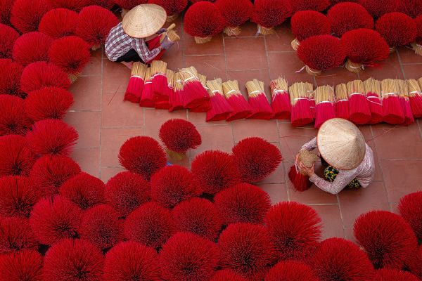 Overhead shot of two people tying thousands of red incense sticks together in Vietnam