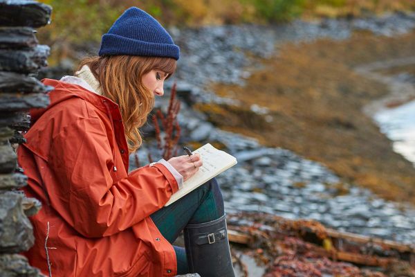 Lady journalling while sitting on rock along water