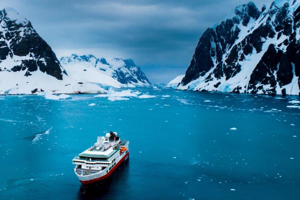 Cruise ship in icy-blue water with snow-capped mountains in background