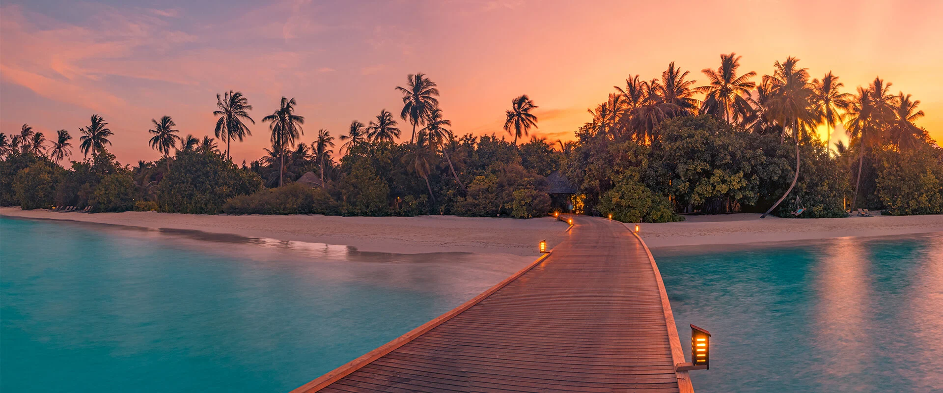 Board walk in the Maldives set over the water with a sunset over the palms