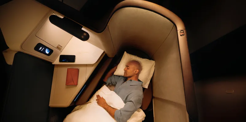 Cathay Pacific business class seat reclined with passenger laying horizontally sleeping with white blanket and pillow.