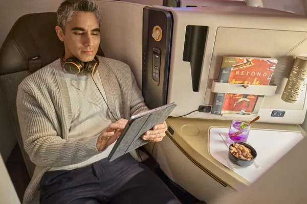 Etihad Airways business class seat with passenger enjoying a beverage and snack while reclining.