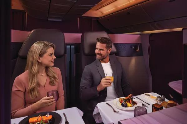 Qatar Airways business class passengers enjoying their meal side-by-side with a beverage in hand.