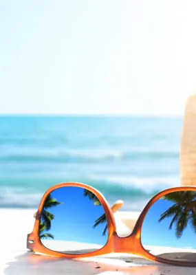 A sunhat and sunglasses sit on a sunny beach