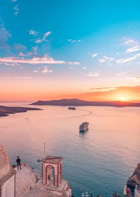 View from the top of Santorini overlooking buildings and the ocean as the sun sets