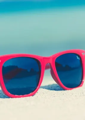 A pair of red sunglasses sitting on a white sand beach