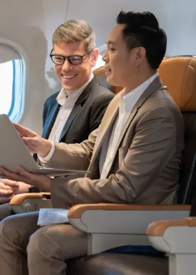 Two men sitting in business class on a plane looking at a laptop together
