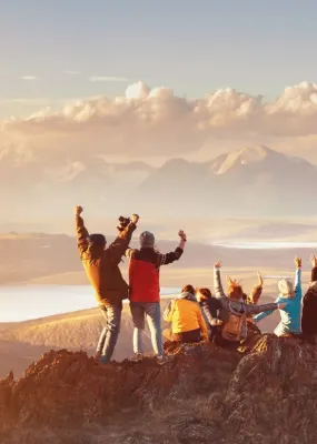 group of friends standing on top of mountain with arms up
