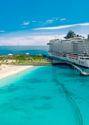 A cruise liner docked at a tropical port with a lighthouse in the foreground