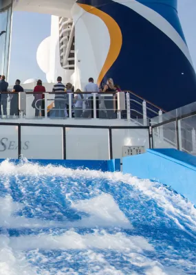 A woman rides the Surf-rider with two people in a skydiving simulator onboard a cruise ship