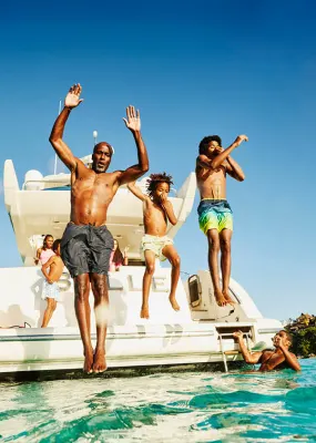 A dad and two kids jumping off the back of a boat into turquoise waters while on a family vacation