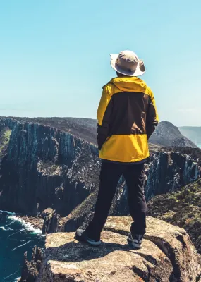 Traveller in a yellow jacket looking out over cliffs by the ocean