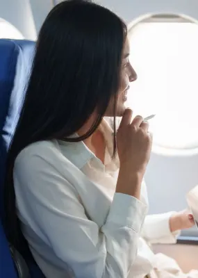 lady holding Ipad and pen under her chin looking out window of plane from business class