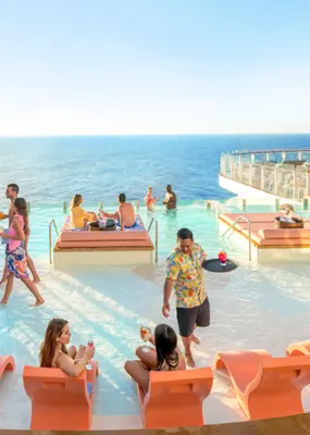 People relax by the pool on a cruise ship deck with ocean views