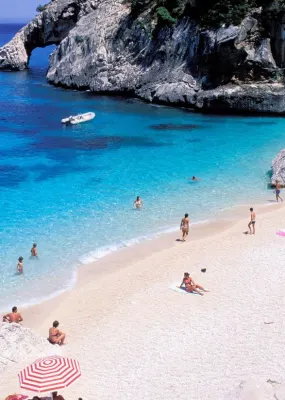 A white sand beach filled with people. Clear blue water with people swimming in it