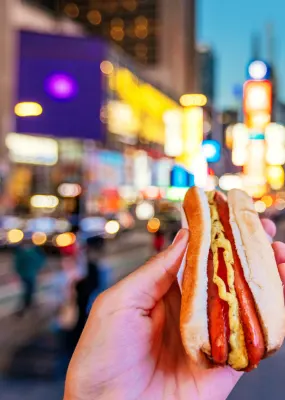 hand holding hot dog with blurred times square in background