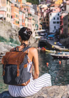 lady sitting on a rock by the water looking at coastal town in Italy