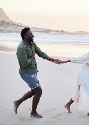 Couple running and laughing while holding hands on beach at sunset