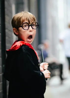 Kid dressed as harry potter holding wand and looking scared