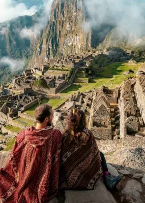 couple sitting on cliff overlooking macchu picchu peru