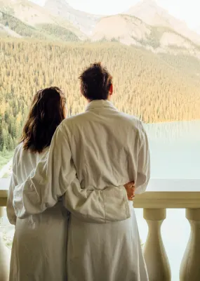 couple standing on balcony in bath robes overlooking mountains and lake in canada