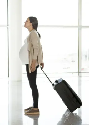 Pregnant woman waiting at the airport with her suitcase 