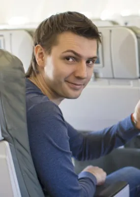 a guy in blue sweaters smiling while giving a thumbs up for a good service on the plane