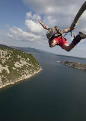 aerial view of a person in red shorts bungee jumping over a river