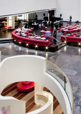 a fancy hotel restaurant with people eating on rounded red couches and waiters serving them