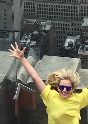 Girl in yellow shirt with her arms up in front of New York buildings 