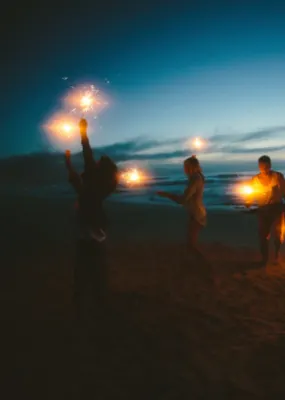 friends happily lighting firework sparklers on the beach at night