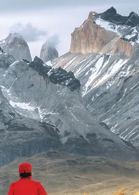 Man in a red winter coat gazing over the snowcapped mountain