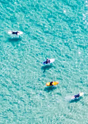 Aerial view of surfers on clear blue beach waters.