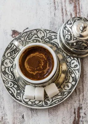 Fortune turkey coffee in an intricately designed cup and saucer with three blocks of white sugar on the side