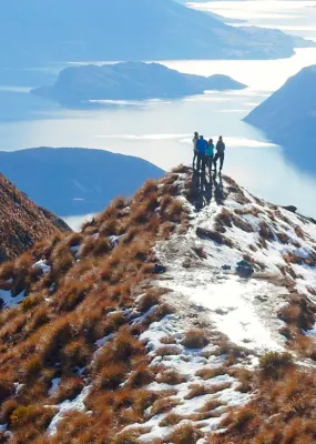 Distant view of hikers standing on a cliff against lake during winter, Queenstown
