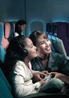 A malaysia Airline flight attendant assisting a curly liitle girl who wants to watch on the led screen at the back of the seat in front of her
