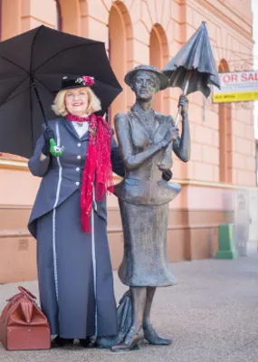 A lady holding a black umbrella and standing beside a lady statue with umbrella