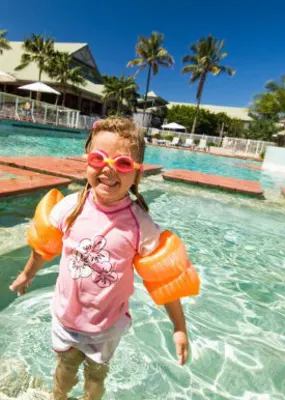 a blonde littel girl in pink shirt and orange floaters enjoying the pool in the Novotel twin waters resort