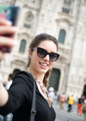 Lady smiling and taking selfie with the Duomo di Milano from behind in Milan, Italy