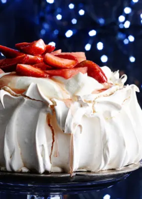 Large, strawberry-topped pavlova on a plate surrounded by small blue lights