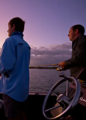 Two men fishing on a boat as the sun sets