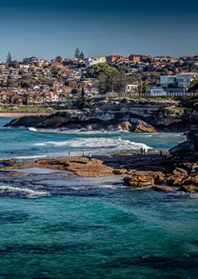Ocean that is part of the Bondi to Cogee walk. Rocks and waves are shown with buildings in the background. 