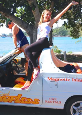 Couple posing on top of a rental car near the beach