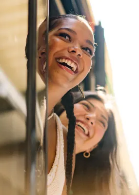 Two women aboard a train; they're looking out of its doors while stopped at a platform