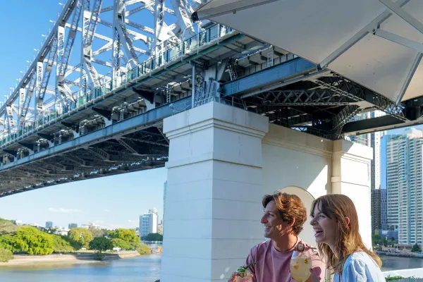 Young couple drinking cocktails sitting under Sydney Harbour Bridge