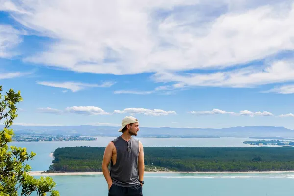 Guy standing on boulder overlooking blue water