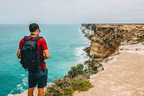 Backpacker standing on the edge of a sandy cliff looking at the waves
